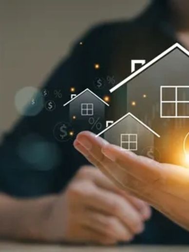 a photo of a hand holding an illustration of a house with a dollar sign glowing.