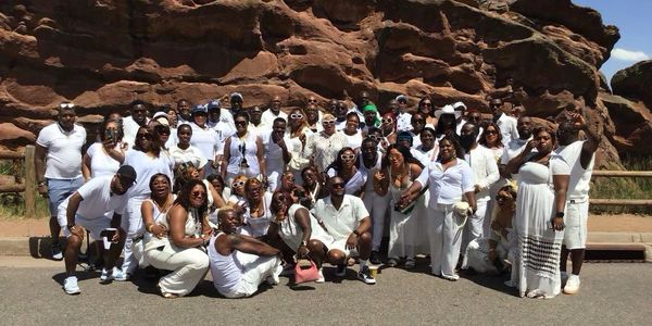 Large group dressed in white posing outdoors near rocky terrain.