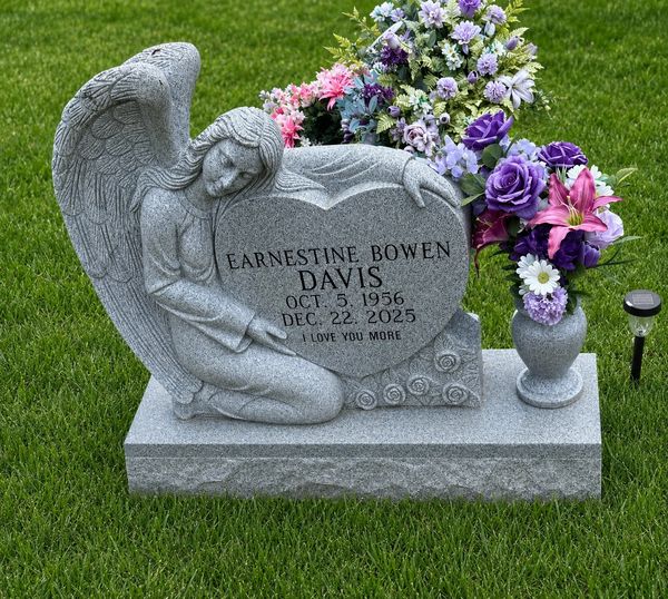 Angel sculpture grave marker with colorful flowers on green grass.
