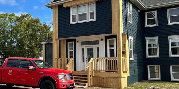 Newly renovated dark blue two-story house with wooden porch and red truck parked outside.