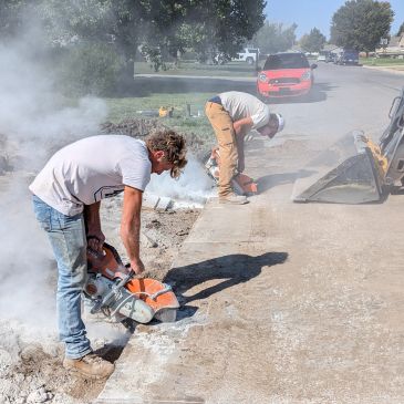 Two construction workers cutting concrete on a sunny day.