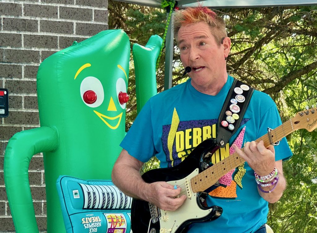 Man playing guitar with inflatable green character.
