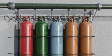 Five colorful gas cylinders connected to a pipe on a wall.