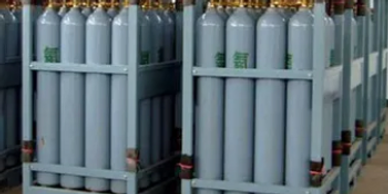 Rows of large industrial gas cylinders stored in metal frames indoors.