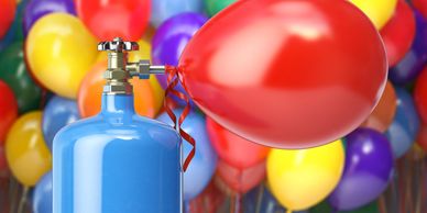A helium tank inflating a red balloon with colorful balloons in the background.