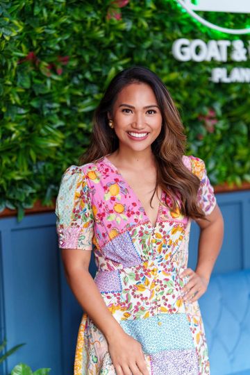 Smiling woman in a colorful floral dress standing indoors.