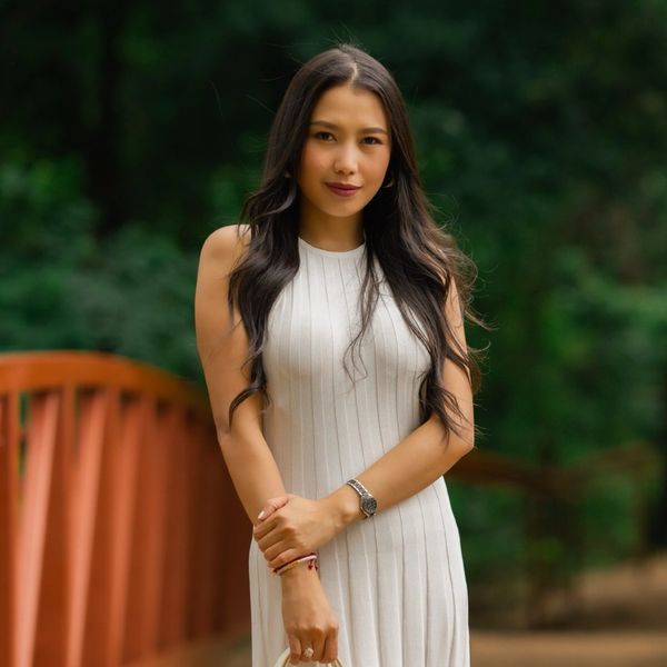 Woman in a white dress stands on a wooden bridge surrounded by greenery.