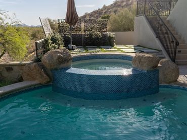 Raised spa with blue mosaic tile surrounded by a newly finished backyard swimming pool.