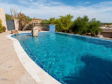 Completed backyard pool remodel with bright blue water, new interior finish and desert landscaping.