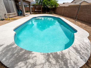 Completed residential swimming pool remodel with fresh decking, blue water and curved pool shape.