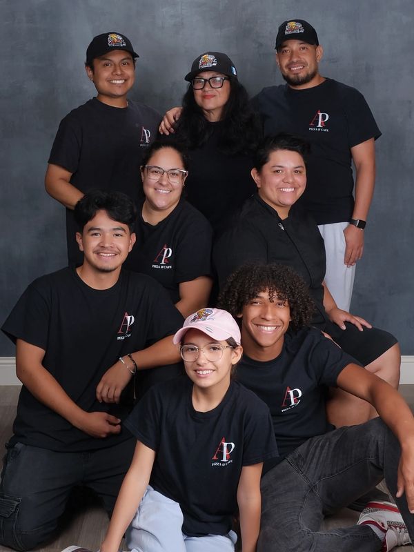 Group of eight smiling people wearing matching AP Pizza & Cafe shirts.