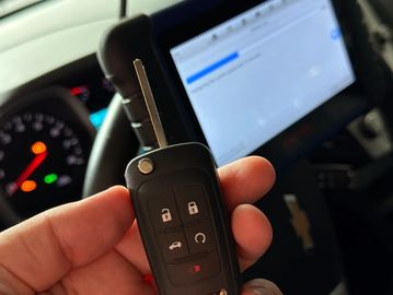 Hand holding a car key with a Chevrolet dashboard in the background.