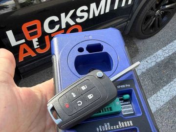 Hand holding a car key and a key programming device in front of a locksmith car.