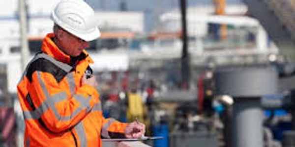 Engineer in safety gear inspecting industrial site with clipboard.