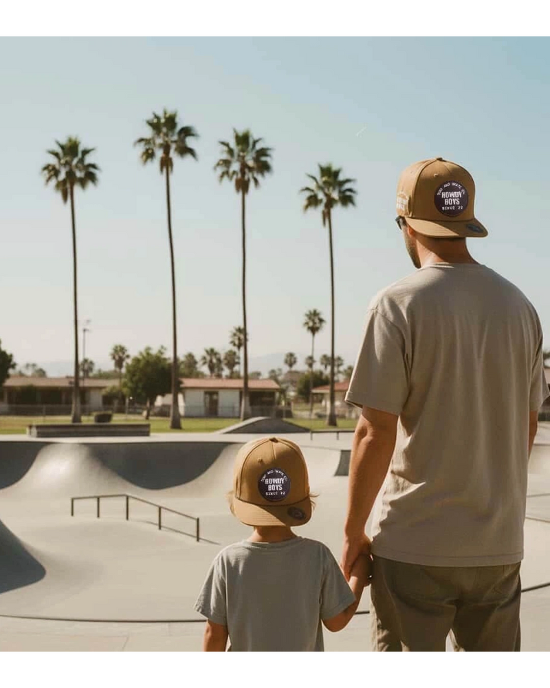 Man holding child's hand while kid rides skateboard at skate park.