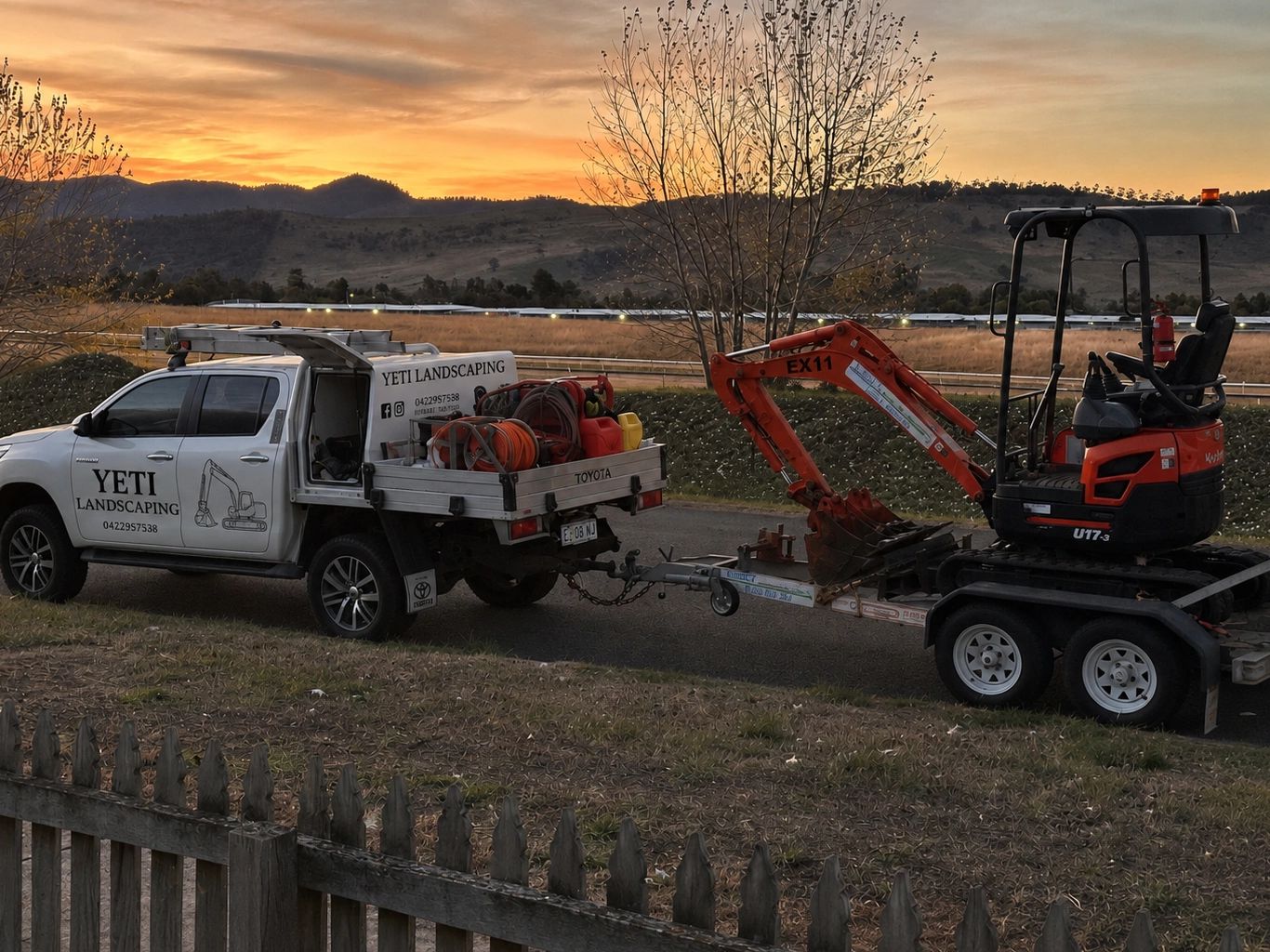 Landscaping truck and excavator at sunset.