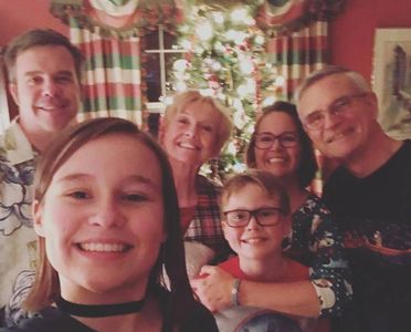 Family smiling together in front of a decorated Christmas tree indoors.