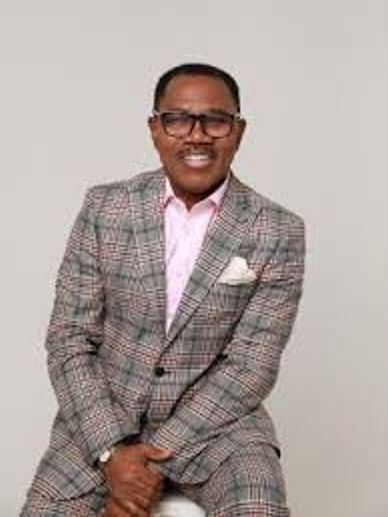 Man smiling in a plaid suit and pink shirt.