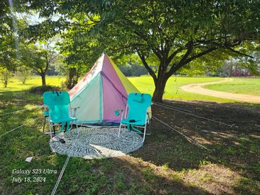 Colorful tent and blue chairs under a large tree on a sunny day.