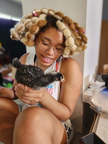 Person with unique hairstyle holding a black bird indoors.