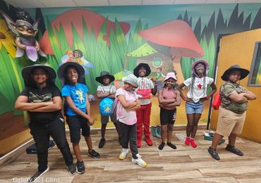 A group of kids posing confidently indoors with colorful fairy-themed mural background.
