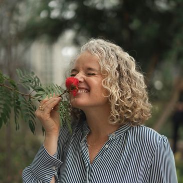 Woman enjoying the scent of a red flower outdoors.