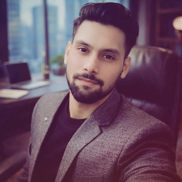 A young man with a beard wearing a gray blazer in an office.