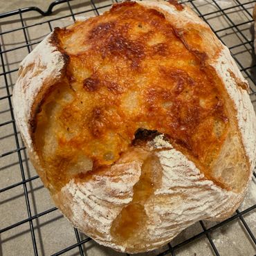 A freshly baked round loaf of crusty bread cooling on a rack.