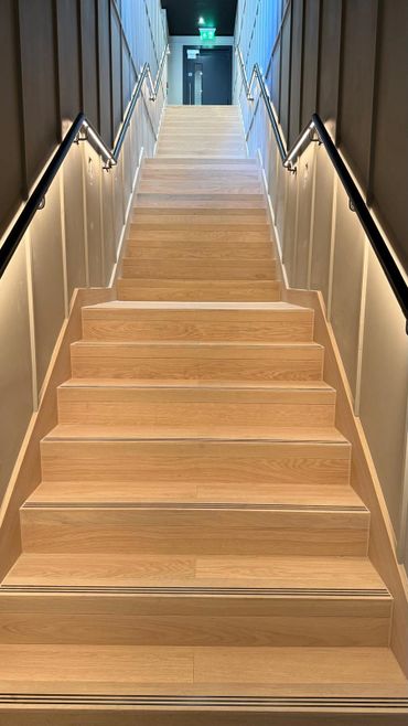 Modern wooden staircase with handrails and LED lighting along the walls.