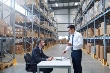 Two men in formal attire discussing work in a warehouse.