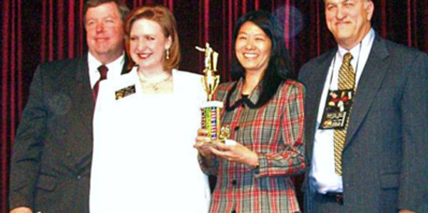 Four people posing with a trophy on stage.