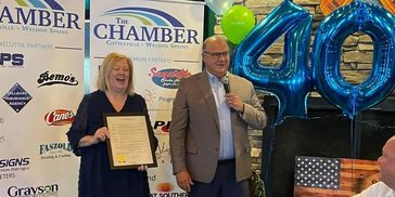 Two people celebrating a 40th anniversary with a certificate and balloons.