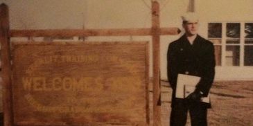 A person in uniform standing next to a wooden welcome sign.