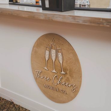 Wooden logo of Three Cheers Mobile Co. on a white bar setup.