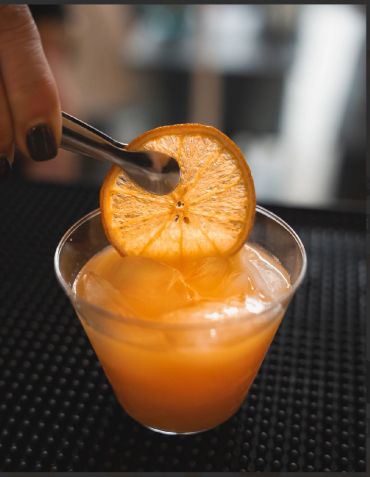 Orange cocktail with ice and dried orange slice garnish.