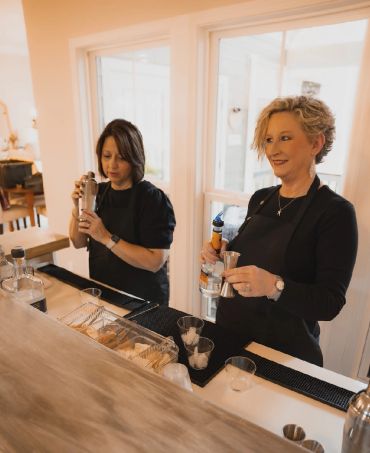 Two women making drinks behind a bar counter.
