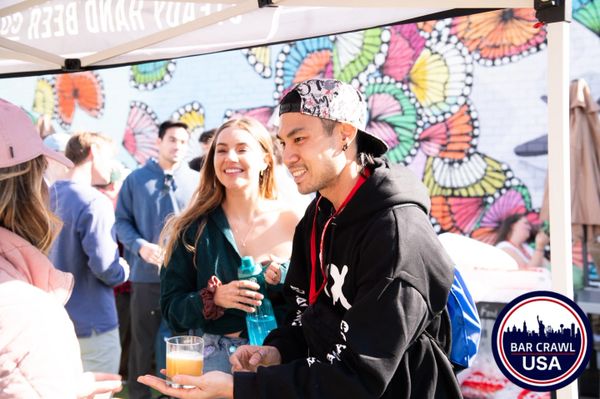 People enjoying a lively outdoor bar crawl event with colorful mural background.