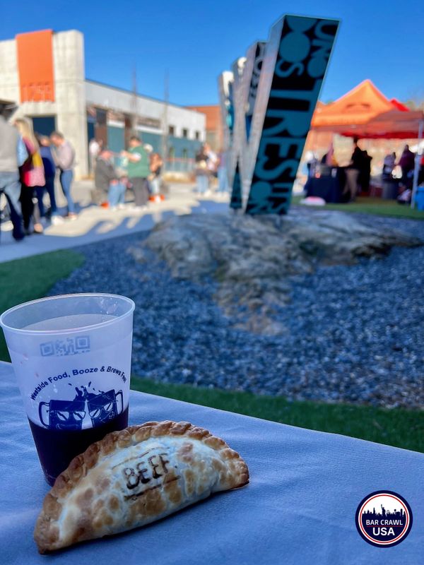 A beef empanada and a drink cup at an outdoor food festival.