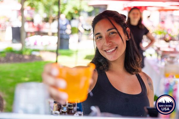 Smiling woman holding an orange drink at an outdoor event.