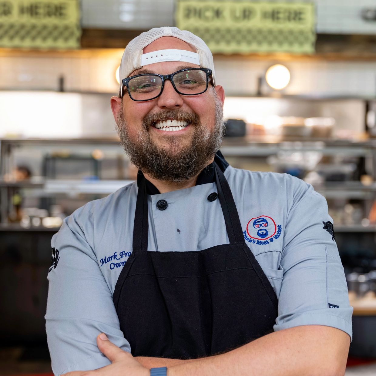 Smiling chef with glasses and a backward cap.