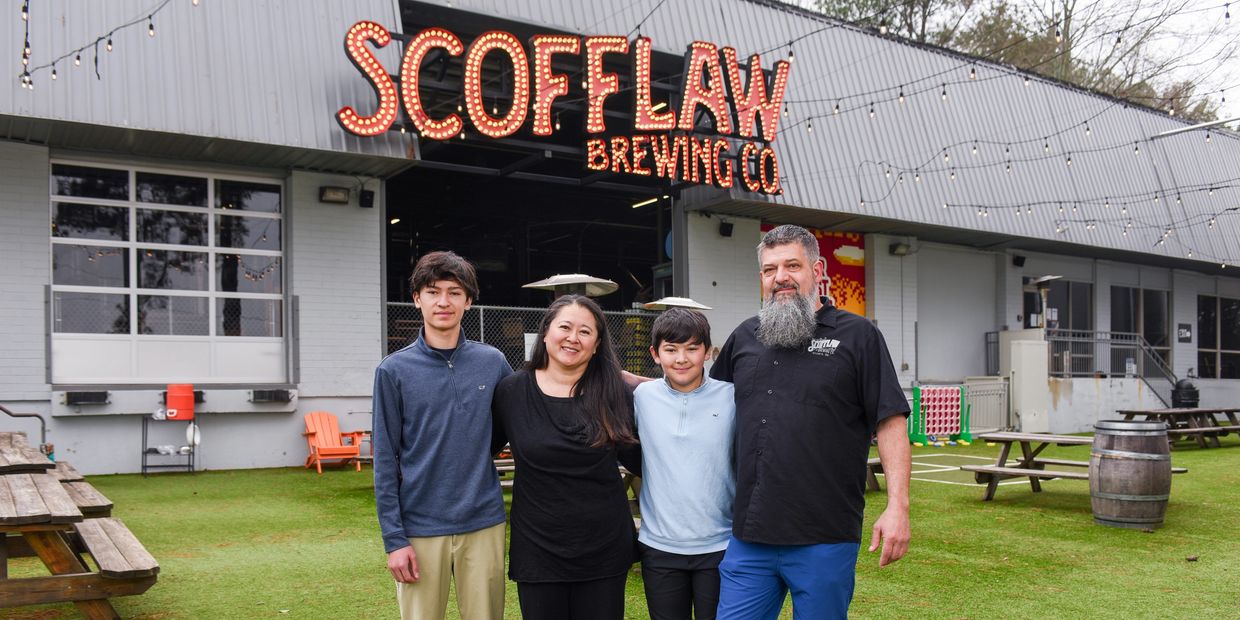 A family of four stands smiling outside Scofflaw Brewing Co on a grassy area.