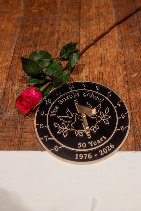 A red rose beside a commemorative sundial on a wooden surface.