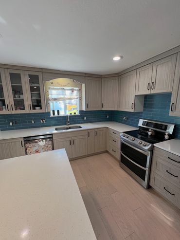 Modern kitchen with light wood cabinets and blue tile backsplash.