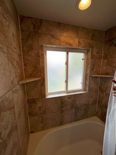 Bathroom with tiled walls, frosted window, and bathtub under ceiling light.