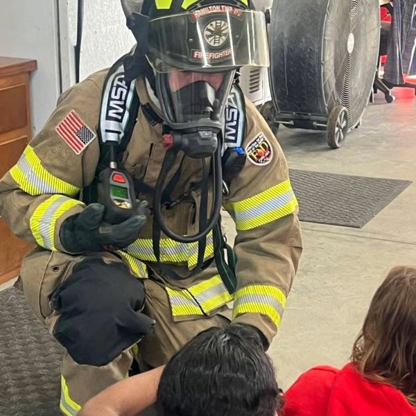 Firefighter in full gear talks to people indoors.