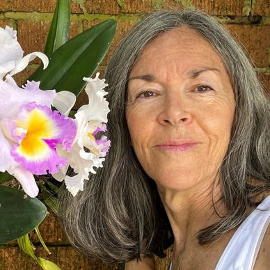 Older woman with gray hair smiles beside a vibrant orchid flower.
