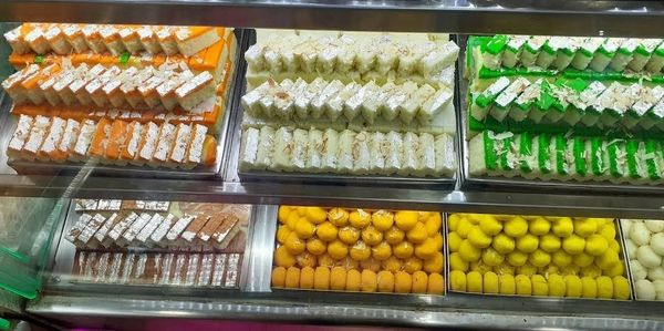 Display of colorful Indian sweets in a glass case.