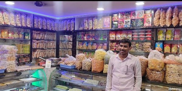 Man standing inside a snack shop filled with various packaged snacks.
