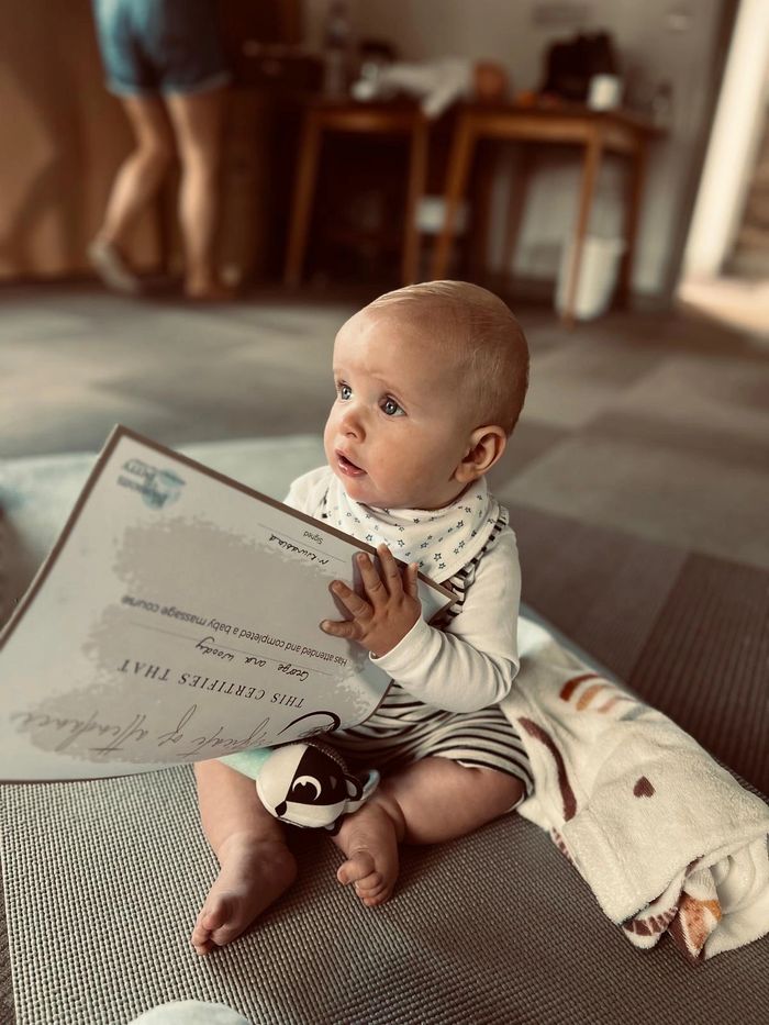 A baby holding a certificate while sitting on a blanket indoors.