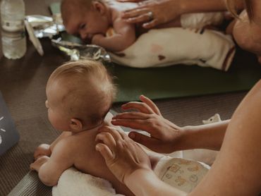 Adults gently massaging babies lying on mats indoors.